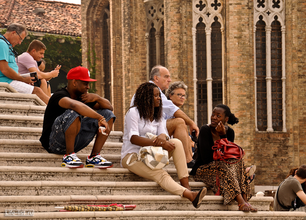 туристы отдыхают на ступеньках собора Санта Мария в Венеции