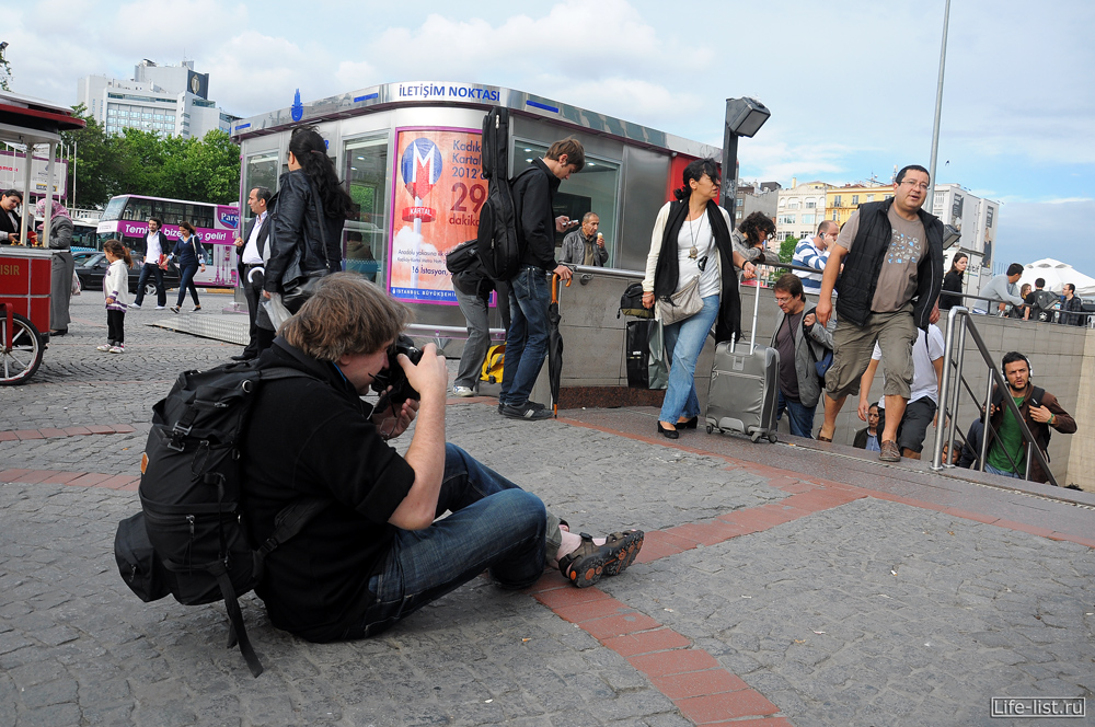 фотограф сидит на асфальте и делает стрит жанр